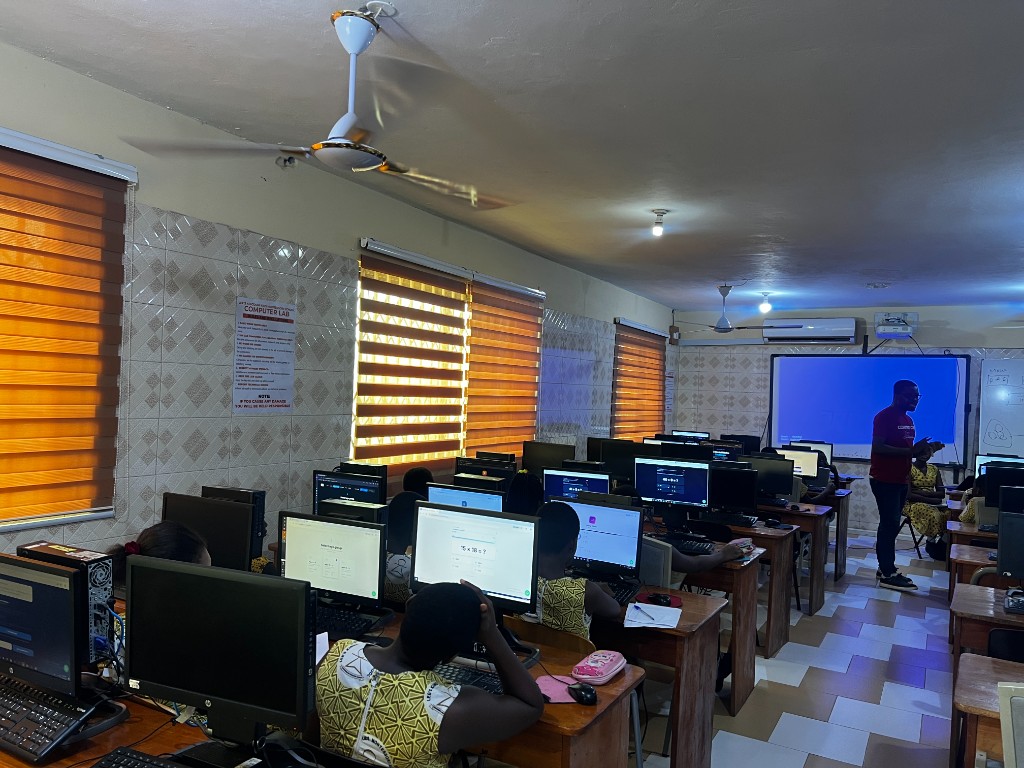Students working through classwork on desktop computers while a Coasted Code instructor teaches from the front of the lab